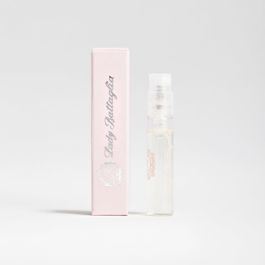 A photo of the Lady Battaglia fragrance sample by Battaglia. The sample is standing upright next to the pink box it is packaged in against a white background.