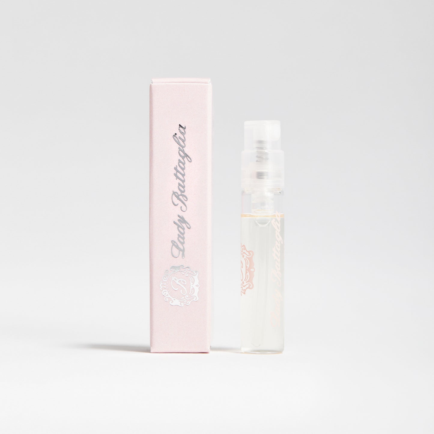 A photo of the Lady Battaglia fragrance sample by Battaglia. The sample is standing upright next to the pink box it is packaged in against a white background. 
