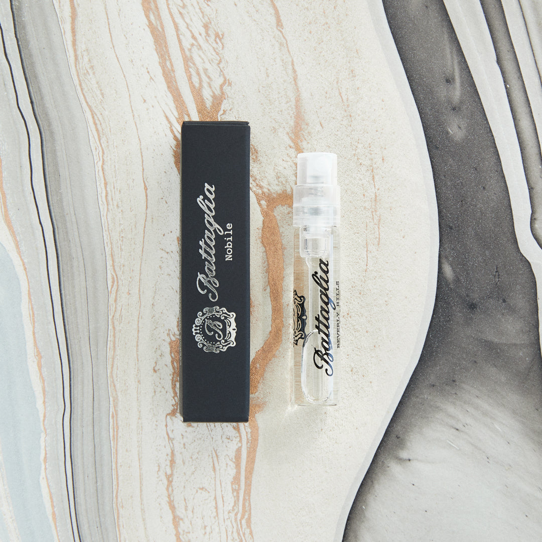 A photo of the Nobile fragrance sample by Battaglia. The sample is standing upright next to the black box it is packaged in against a marbled paper background.