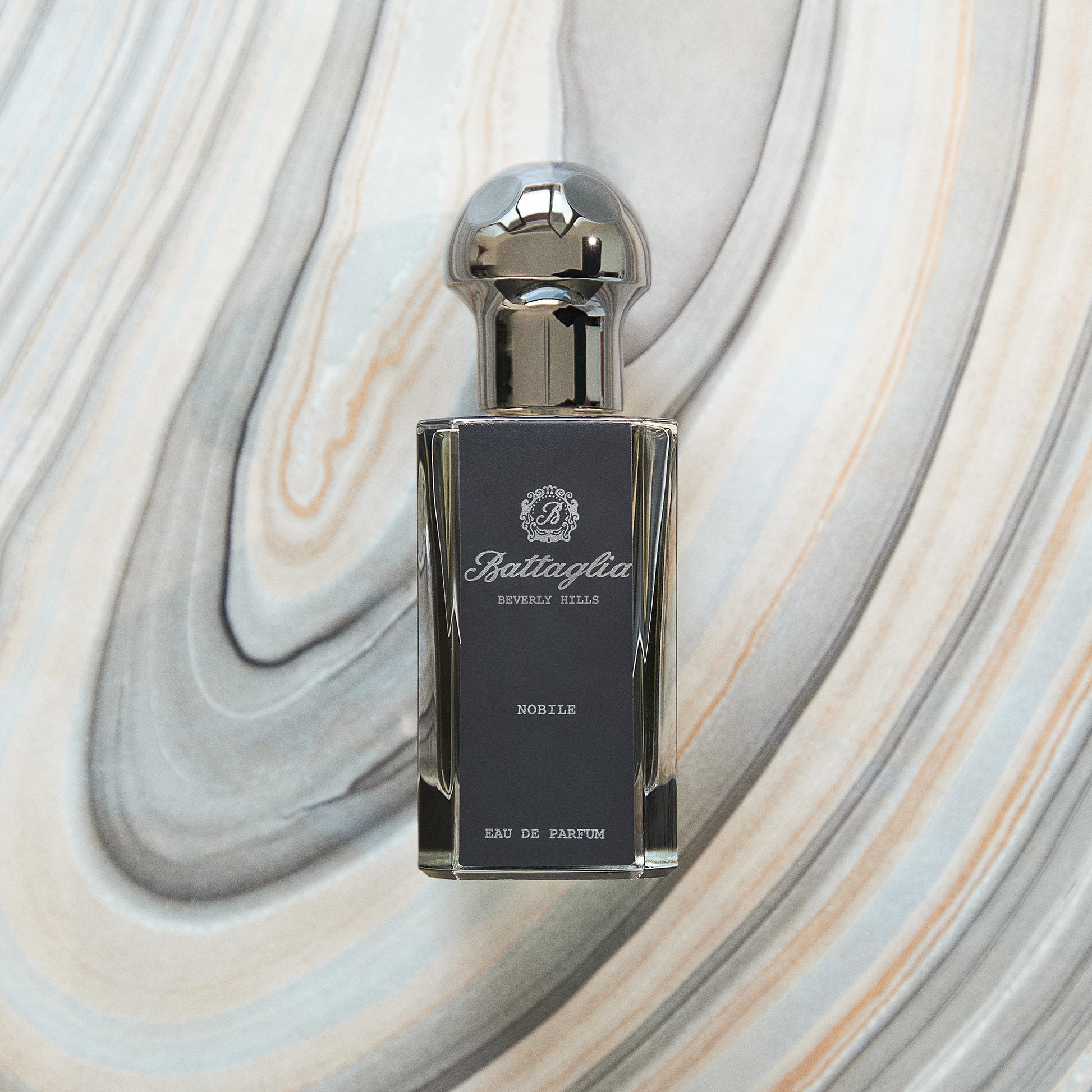 A photo of the Nobile fragrance by Battaglia against a grey marbled paper background.  The bottle is rectangular and black with a grey circular top. 